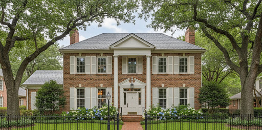 Classic two-story Georgian Colonial brick home with white pilasters, pediment entry, louvered shutters, and twin chimneys, framed by mature live oak trees, an iron fence, and a colorful border of blue and white hydrangeas along a brick walkway.
